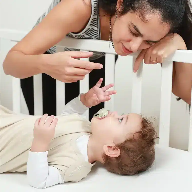 אמא רכונה מעל מיטת התינוק, התינוק שוכב על הגב עם מוצץ